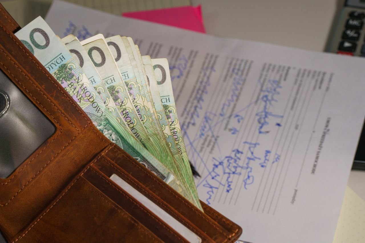 about-us Close-up of a wallet containing Polish Zloty with a signed document in the background, representing financial transactions.