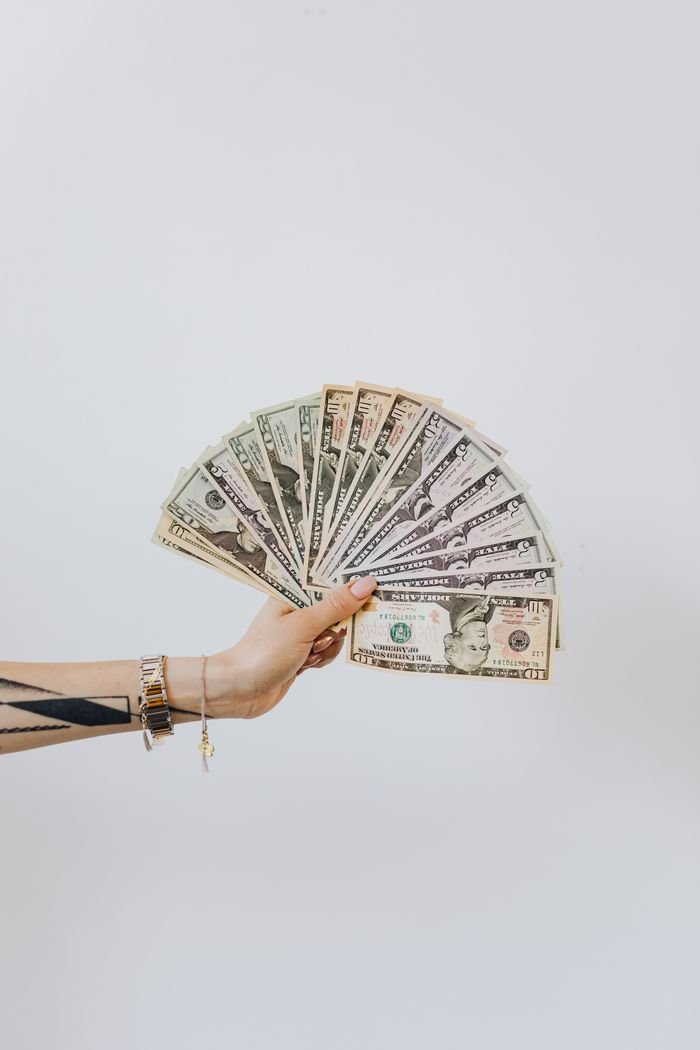Close-up of a hand displaying fanned out US dollar bills against a white background.